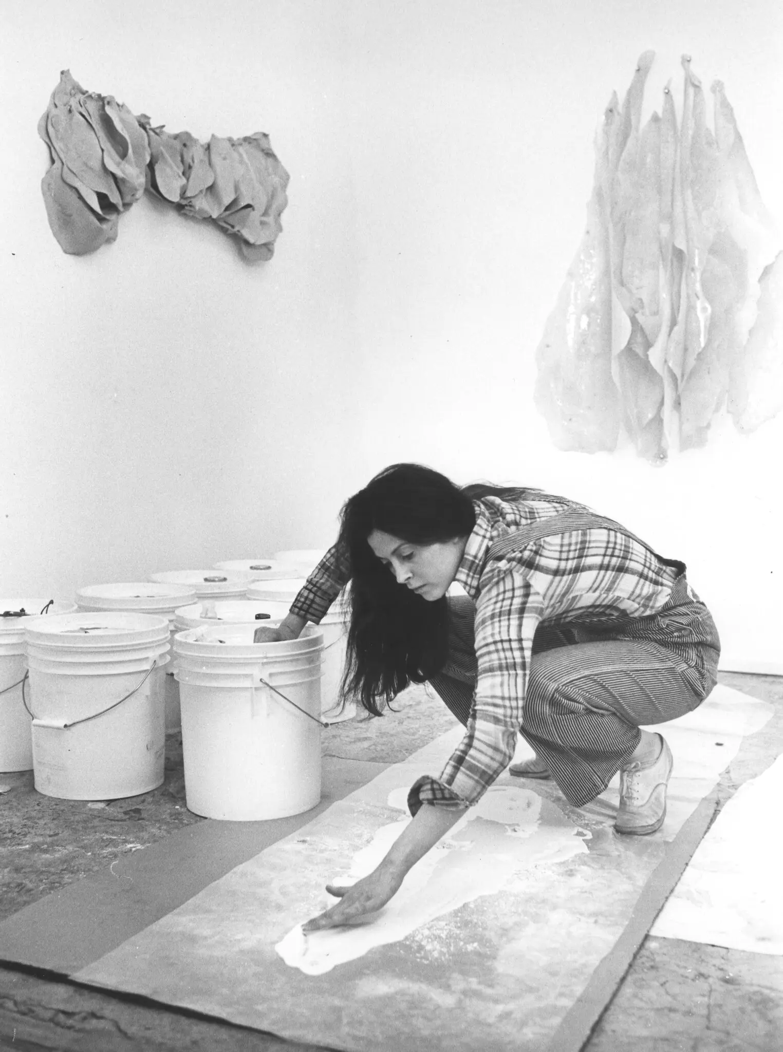 Hannah Wilke despejando látex em seu estúdio na Broome Street, 1974, com “Bow-Tie Bone,” 1972 (esquerda), e “Untitled,” 1971 (direita). Seu trabalho é mais provocativo, caracterizado por formas dobradas que lembram o corpo feminino. (Crédito da fotografia: Cortesia © Copyright All Rights Reserved/ © Marsie, Emanuelle, Damon e Andrew Scharlatt, Hannah Wilke Collection & Archive, Los Angeles e Alison Jacques Gallery, Londres/Licenciado pela VAGA na Artist's Rights Society (ARS), NY/ REPRODUÇÃO/ TODOS OS DIREITOS RESERVADOS)