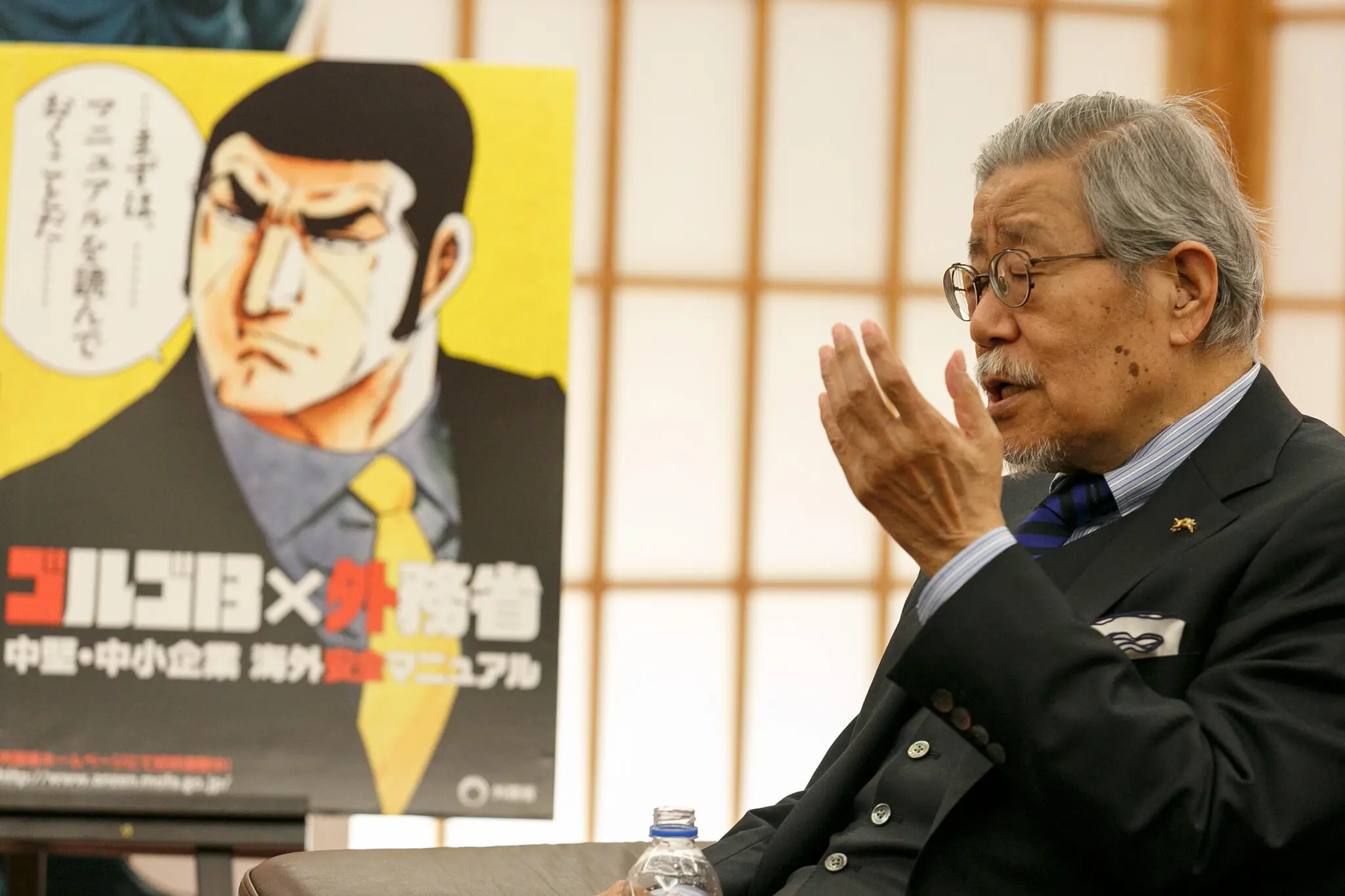 O Sr. Takao Saito em um evento em 2017 em homenagem à sua longa série “Golgo 13”. Seu anti-herói está no pôster atrás dele. (Crédito da fotografia: cortesia Aflo Co. Ltd./Alamy Notícias ao vivo)