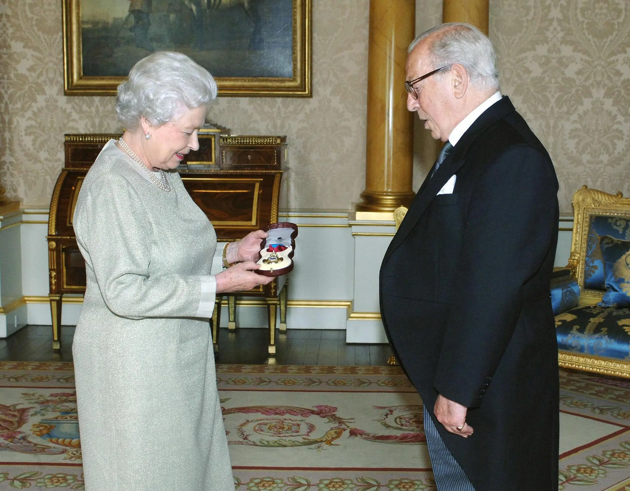 A Rainha Elizabeth II concede a Michael Howard a Insígnia da Ordem do Mérito em 2005. “Tive que aprender não apenas a pensar sobre a guerra de uma maneira diferente, mas também a pensar sobre a história em si de uma maneira diferente”, ele escreveu certa vez.Crédito...Imagens da PA, via Getty Images